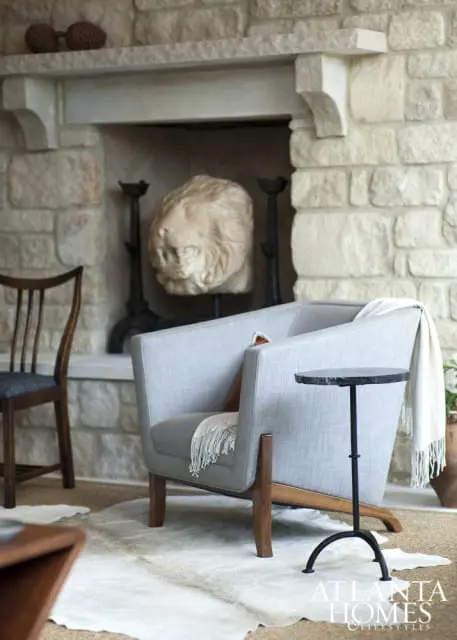 Living room with a stone fireplace, a light gray upholstered armchair with wooden legs, a dark wood chair, and a small black side table.