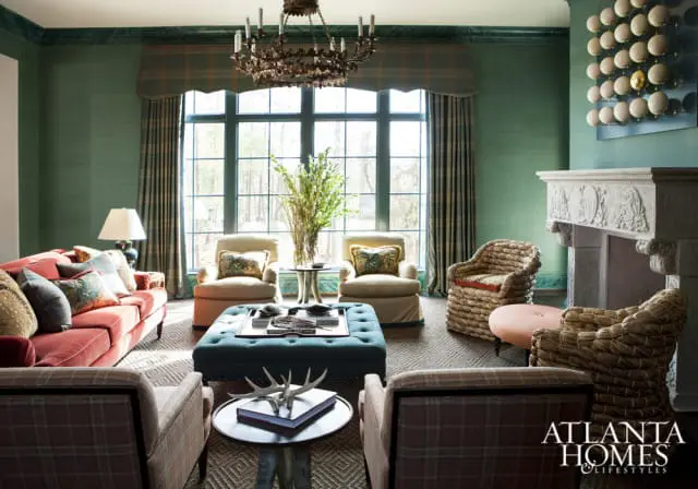Living room with green grasscloth wallpaper, a coral sofa, plaid armchairs, woven chairs, a teal tufted ottoman, and a stone fireplace.
