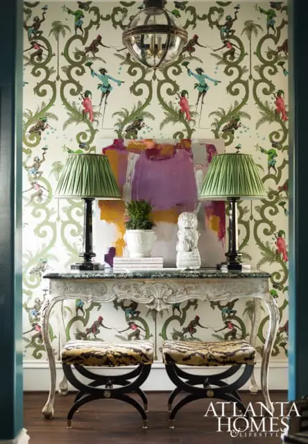 Entryway with bold figural wallpaper, a marble-topped console table with two green lamps, abstract art, and two tiger-print stools.