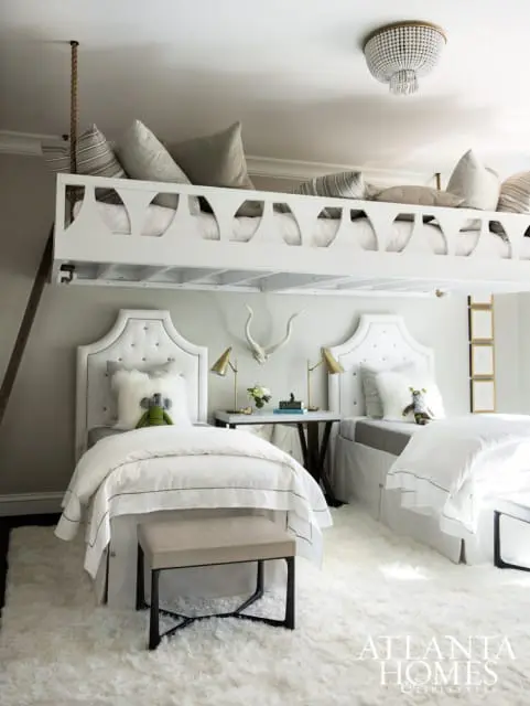 Children's bedroom with two twin beds, white tufted headboards, and a white loft bed with decorative cutouts above.