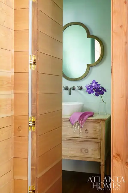 Powder room with light blue walls, a clover-shaped mirror, a white vessel sink, and a distressed wood vanity with a purple towel.