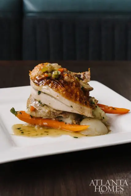 Stack of sliced roasted chicken with glazed carrots and mashed potatoes on a white plate, topped with diced vegetables and gravy.