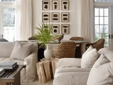 Living room with linen sofas, woven chairs, glass dining table, and wall art.