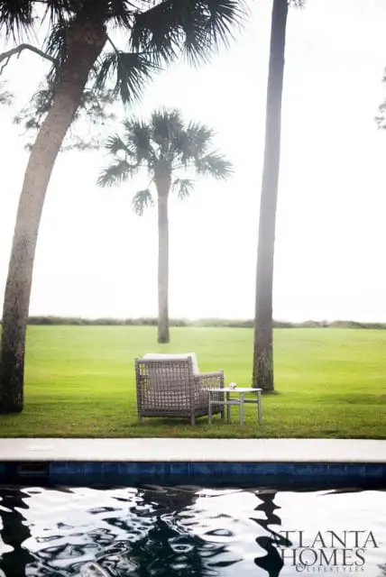 Wicker armchair and side table on a green lawn with palm trees and a swimming pool in the foreground.