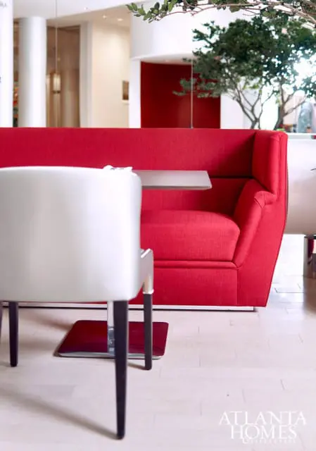 Modern dining area with a bright red upholstered booth seating and a white chair with chrome legs. A small gray table is attached to the booth.
