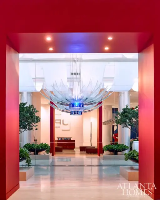 Modern lobby with a large, lotus-shaped glass chandelier with blue LED lights, red columns, and glass partitions.