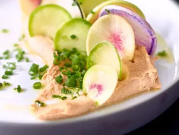 Close-up of a dish with a dollop of hummus, topped with thinly sliced radishes and green onions, drizzled with oil.
