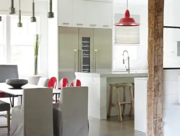 Modern kitchen and dining area with stainless steel appliances, white cabinetry, a marble island, and a dining set featuring gray upholstered chairs and a bench with red accents.