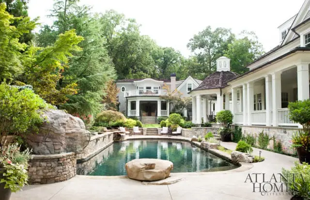 Luxury backyard with a freeform pool, stone retaining walls, lush landscaping, and a multi-story home with a wraparound porch.