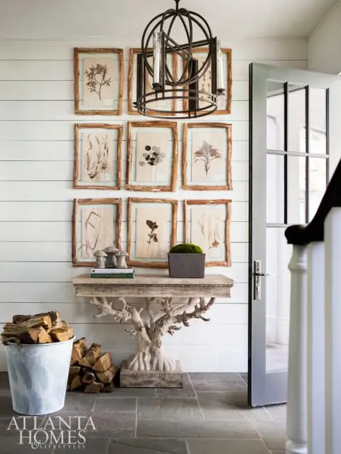 Entryway with shiplap walls, a gallery wall of botanical prints in rustic frames, a sculptural console table, and a metal orb chandelier.