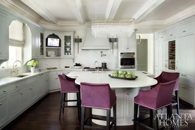 Light gray kitchen with white marble countertops, a large island with purple velvet bar stools, and a crystal chandelier.