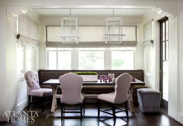 Dining nook with upholstered banquette seating, tufted lilac chairs, and a dark wood table set with purple glassware and a moss centerpiece.