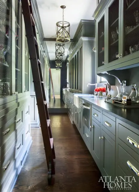 Dark gray kitchen with a rolling ladder, mesh cabinet doors, and modern pendant lights.