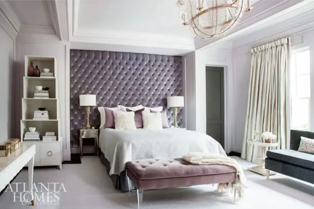Bedroom with a large tufted purple headboard, white bedding, a purple velvet bench, and a crystal chandelier.