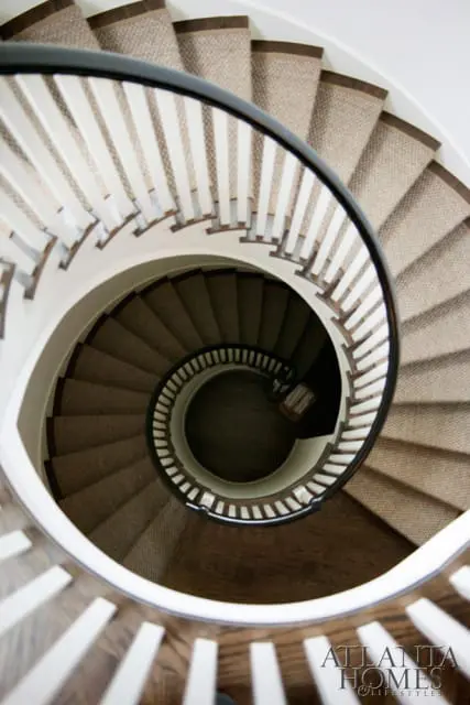 Spiral staircase with neutral patterned carpet, white balusters, dark wood handrail, and dark wood flooring