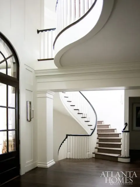 Foyer with dark wood floors, a grand curved staircase with white balusters and dark railing, and a dark wood door with arched glass panes.