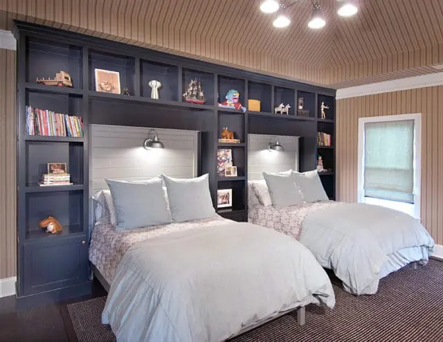 Children's bedroom with two beds, navy built-in bookshelves, light blue bedding, and striped wallpaper.