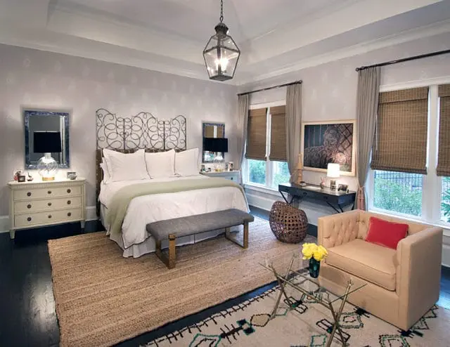 Guest bedroom with a tufted cream armchair, glass coffee table, jute rug, and a metal-frame bed with white linens and a pale green throw.