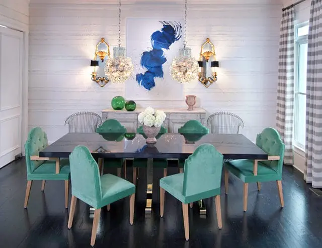 Dining room with teal velvet upholstered chairs around a dark wood table, striped curtains, and abstract blue wall art.
