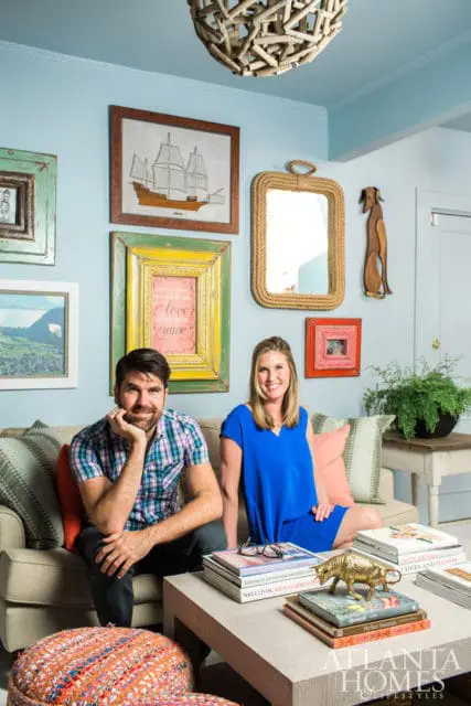 Man and woman sitting on a couch in a light blue room with eclectic wall art, including a ship painting and a rope-framed mirror.