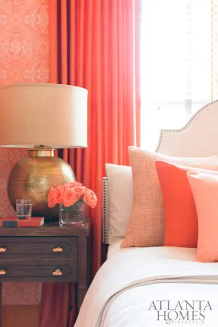 Bedroom with coral wallpaper, coral curtains, a gold textured lamp, and a bed with coral and white pillows.