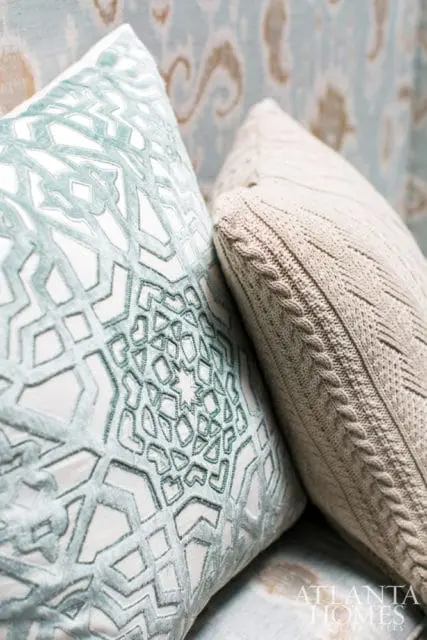 Close-up of two decorative pillows: one with a teal geometric pattern on white, the other a cream cable knit.