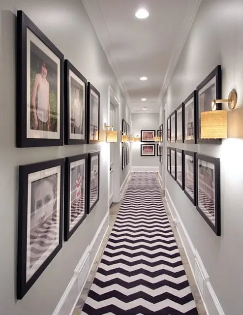 Hallway with light gray walls, black framed portraits, chevron patterned runner, and wall-mounted sconces with woven shades