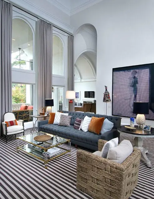 Gray tufted sofa with assorted throw pillows on a striped rug in a living room with high arched windows and vaulted ceilings.
