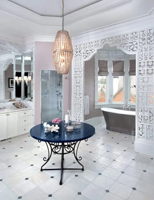 Master bathroom with marble tile floor, white cabinetry, freestanding tub, glass shower, and a dark blue round table with a crystal chandelier above.