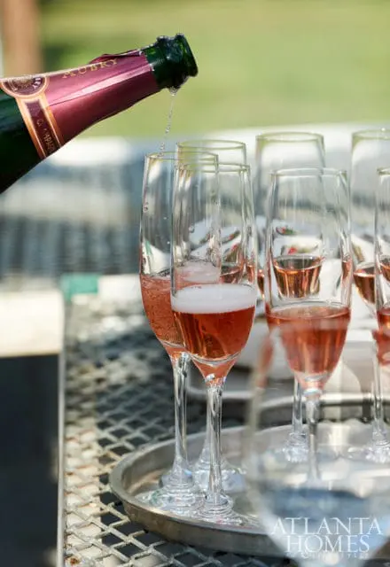 Champagne being poured from a bottle into flute glasses filled with rosé champagne.