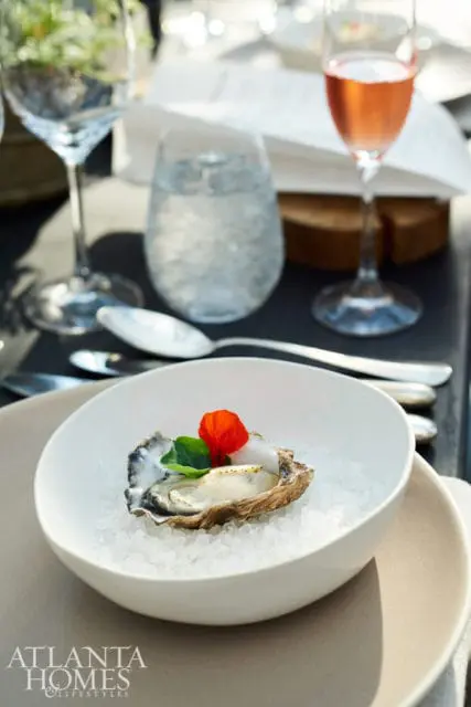 Oyster served on crushed ice in a white bowl, garnished with a red flower petal and green leaves.