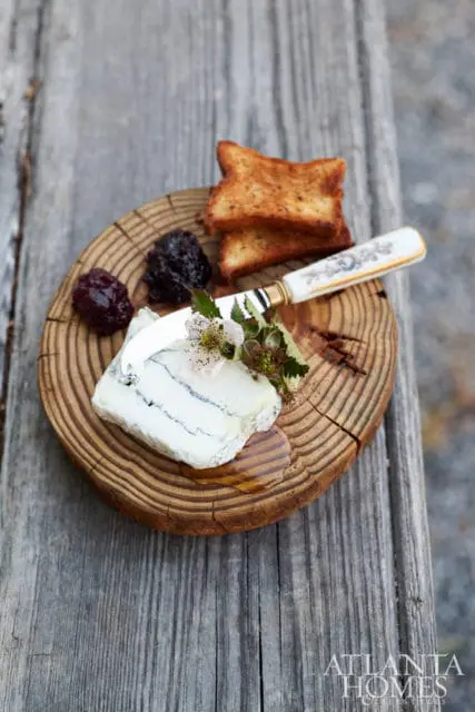 Slice of blue-veined cheese with jam and toast on a wooden board, drizzled with honey, with a decorative knife.