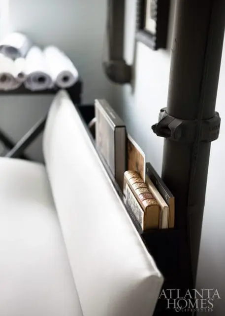 White upholstered bench with a built-in black shelf holding books and a dark metal pipe fixture.