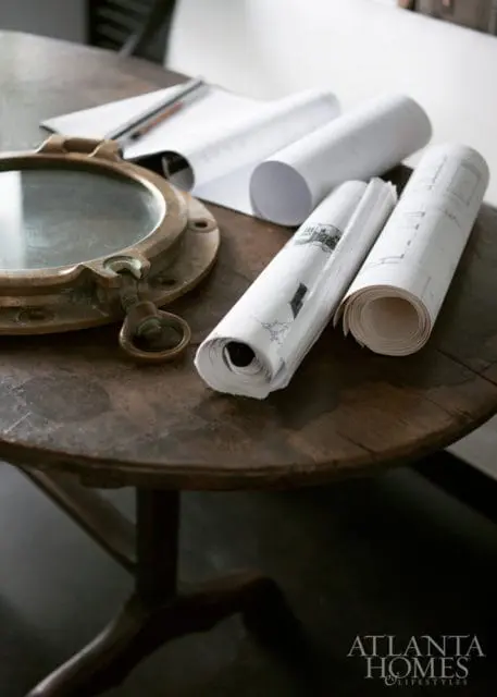 Brass porthole and rolled blueprints on a dark wooden table.