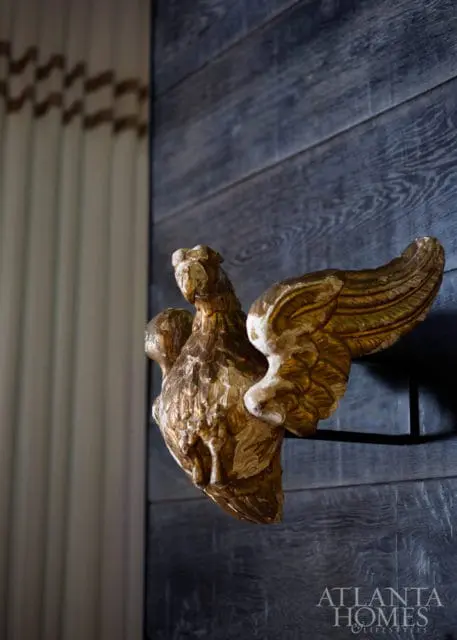 Gold gilded mythological creature sculpture mounted on dark wood plank wall, with striped curtains visible on the left.