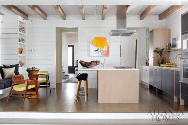 Modern kitchen with white shiplap walls, exposed wooden beams, a light wood island with a gas stovetop, and dark grey lower cabinets.