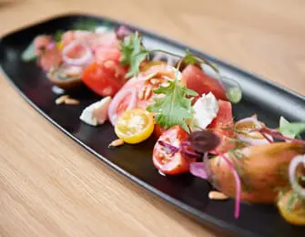 Heirloom tomato salad with feta cheese, red onion, microgreens, and pine nuts on a black platter