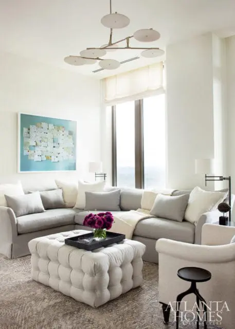 Living room with a large sectional sofa in light gray, a tufted ottoman, and a modern chandelier. A large artwork hangs on the wall above the sofa.