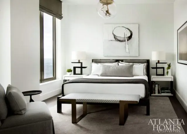 Modern bedroom with a king-size bed, gray bedding, abstract art, and a large window.