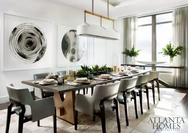 Modern dining room with a long concrete table set for a meal, light gray upholstered chairs, and large circular abstract art on the wall.