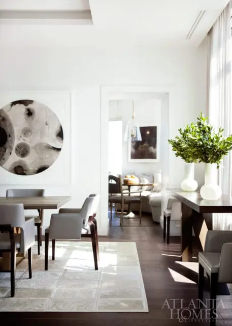 Modern dining room with a large abstract circular artwork on the wall, a wooden dining table with grey upholstered chairs, and a textured rug.
