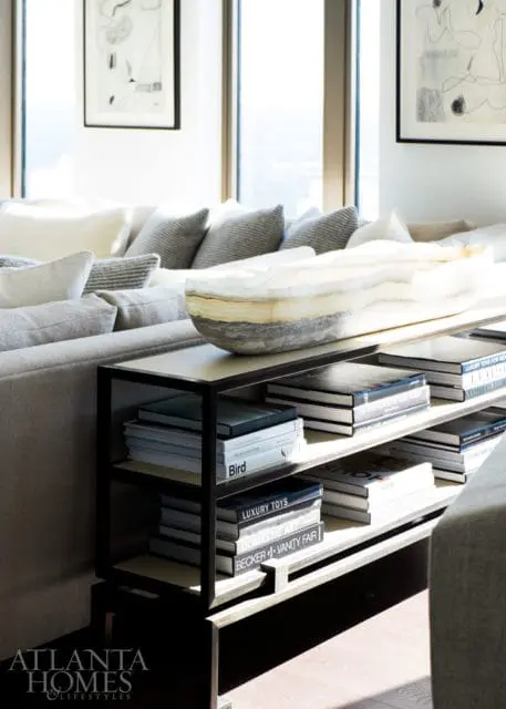 Living room with neutral-toned sectional sofa, patterned throw pillows, and a console table displaying books and a large decorative bowl.