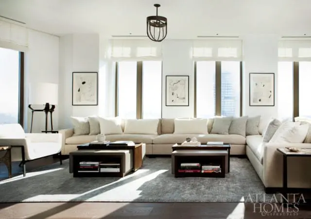 Modern living room with a large sectional sofa, two nesting coffee tables, abstract art, and floor-to-ceiling windows.