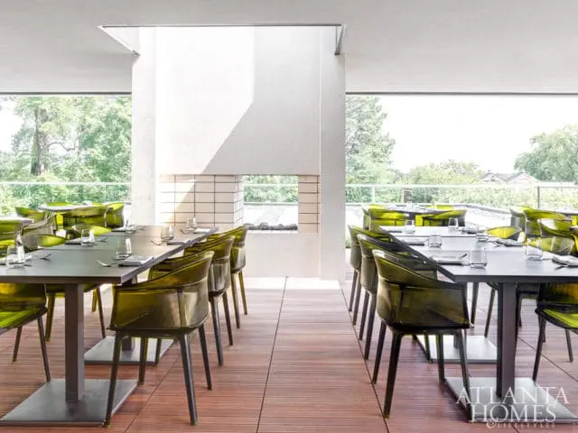 Restaurant dining area with dark tables set with glassware and cutlery, surrounded by translucent green chairs, overlooking an outdoor view.