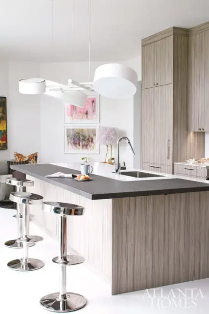 Modern kitchen with a large gray island, light wood cabinetry, and chrome bar stools. A contemporary white chandelier hangs overhead.