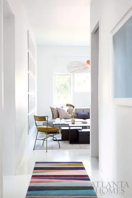 Hallway with a colorful striped rug leading to a living room with a gray sofa, black coffee table, and modern pendant light.