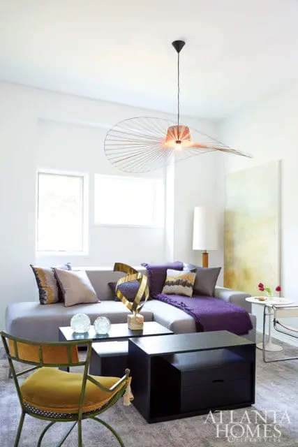 Living room with a gray sectional sofa, purple throw blanket, patterned pillows, and a large, unique pendant light.