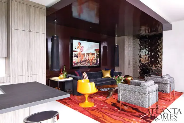 Living room with dark gray tufted sofa, two gray upholstered armchairs, a bright yellow accent chair, and a large abstract red and orange rug. A framed artwork hangs above the sofa, and a glossy dark red ceiling reflects the room.