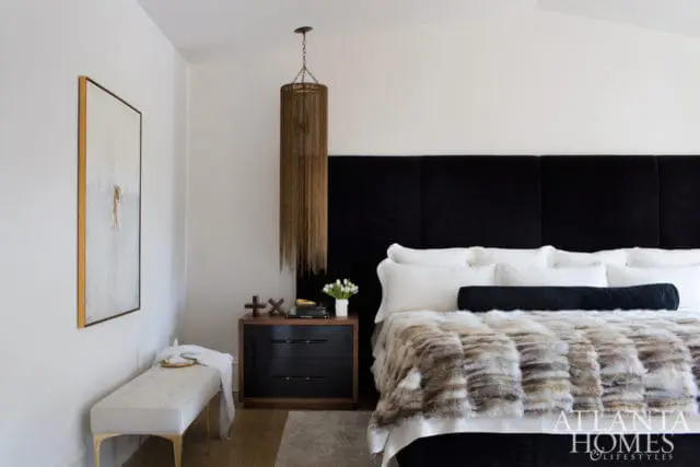 Bedroom with white walls, black upholstered headboard, and a plush fur throw on the bed. A gold-framed abstract painting hangs on the wall.
