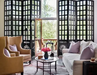 Living room with two upholstered chairs, a sofa, and a large black folding screen with glass panes. A vase of pink flowers sits on a coffee table.